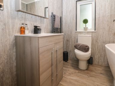 A bathroom with a wooden vanity unit sink soap dispensers toilet with a rolled towel and a small plant on the window sill at Ruperts Retreat in Nateby near Garstang