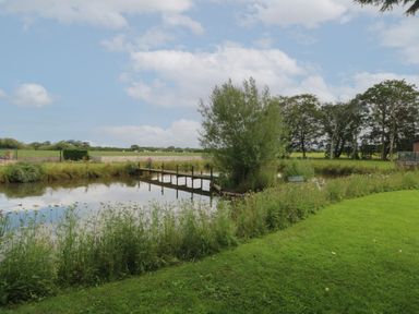 A pond with a wooden dock surrounded by grass and trees at Ruperts Retreat in Nateby near Garstang
