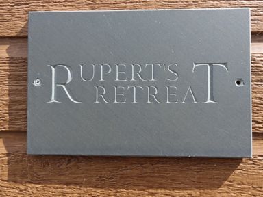 A rectangular stone sign with the words Ruperts Retreat engraved mounted on a wooden surface at Ruperts Retreat in Nateby near Garstang