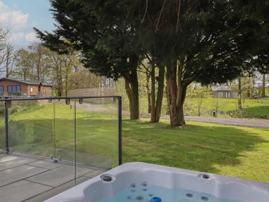A hot tub on a patio overlooking a grassy area with trees and houses at Ruperts Retreat in Nateby near Garstang
