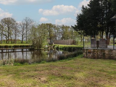 A grassy yard with a pond surrounded by trees and a patio area with outdoor furniture at Ruperts Retreat in Nateby near Garstang