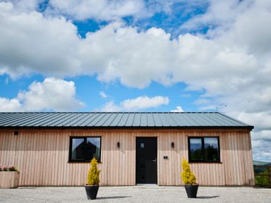 Front view of a wooden building with two windows a black door and two potted plants at Ingleborough Lodge in Rathmell near Settle