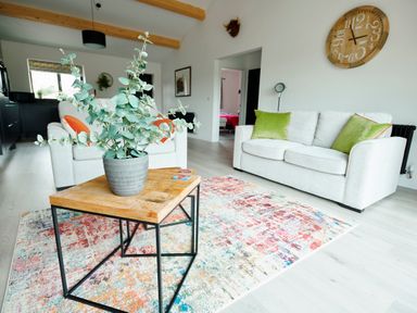 A living room with two white sofas green and orange cushions a wooden coffee table with a plant and a wall clock at Ingleborough Lodge in Rathmell near Settle