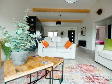 A living room with a wooden coffee table with a plant a white sofa with orange cushions and a black kitchen unit at Ingleborough Lodge in Rathmell near Settle