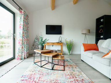 A living room with a sofa cushions colorful rug nested tables and a TV on the wall at Ingleborough Lodge Rathmell near Settle