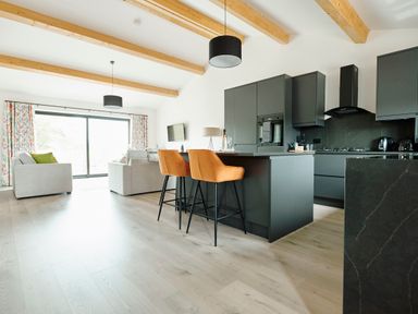 An open kitchen and living area with dark cabinets orange bar stools grey sofas and large sliding glass door at Ingleborough Lodge Rathmell near Settle