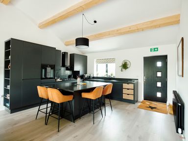 A kitchen with black cabinets an island with four orange bar stools and a black door at Ingleborough Lodge in Rathmell near Settle