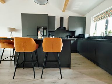 A modern kitchen with black cabinets orange bar stools a black island and kitchen appliances at Ingleborough Lodge in Rathmell near Settle