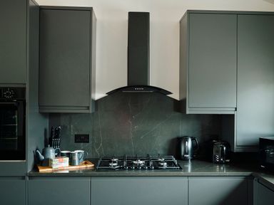 A kitchen with a gas stove a black oven grey cabinets a kettle toaster and cutting board at Ingleborough Lodge in Rathmell near Settle