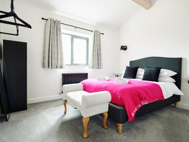A bedroom with a bed with pink blanket and black pillows a window with curtains and a bench at Ingleborough Lodge in Rathmell near Settle