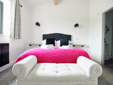 A bedroom with a bed covered in a pink blanket two black pillows a light gray upholstered bench and curtains at Ingleborough Lodge in Rathmell near Settle