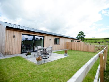A wooden house with a patio table and chairs on a stone patio in a fenced grass yard at Ingleborough Lodge in Rathmell near Settle