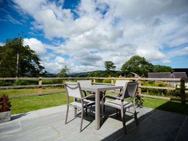 An outdoor patio with a table and four chairs overlooking a fenced grassy yard and distant hills at Ingleborough Lodge in Rathmell near Settle