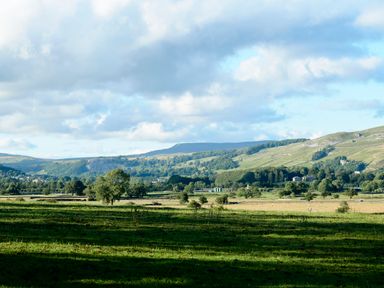 A rural landscape with green fields trees and hills under a partly cloudy sky at Ingleborough Lodge in Rathmell near Settle