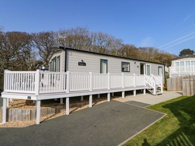A static caravan with a white deck railing and steps surrounded by trees at Crosswinds 68 in Bembridge
