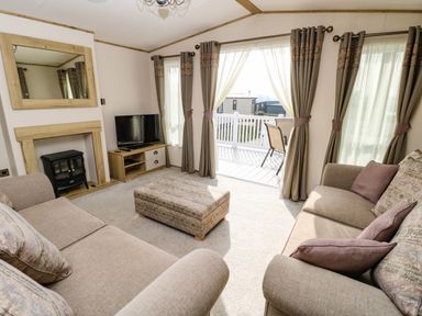 A living room with two sofas a pouf tv and a fireplace with mirror at Crosswinds 68 in Bembridge