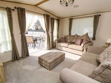 A living room with two sofas an ottoman and patio doors leading to a deck at Crosswinds 68 in Bembridge