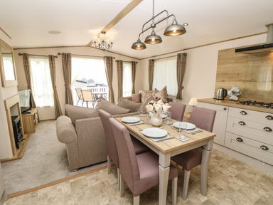 A dining table with plates and glasses next to a living area with sofas and a fireplace at Crosswinds 68 in Bembridge