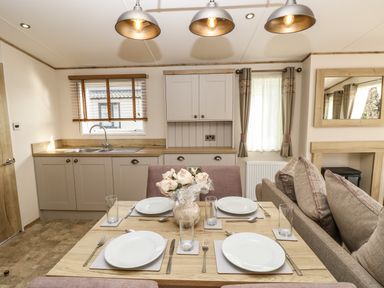 A dining table set for four with plates and glasses near a small kitchen and a sofa at Crosswinds 68 in Bembridge