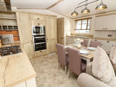 A kitchen and dining area with wooden cabinets a dining table set for four and a gas stove at Crosswinds 68 in Bembridge