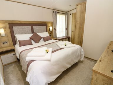 A bedroom with a double bed with pillows and towels beside a window and wooden furniture at Crosswinds 68 in Bembridge