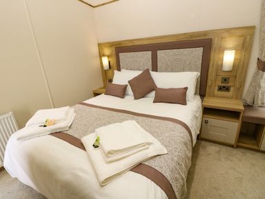 A bedroom with a bed with white linens and brown patterned runner and cushions at Crosswinds 68 in Bembridge