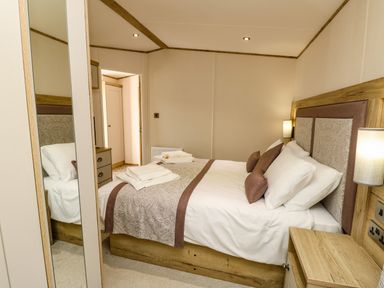 A bedroom with a bed made with white and patterned linens bedside tables and a wardrobe with mirrored doors at Crosswinds 68 in Bembridge