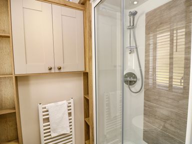 A bathroom with a glass shower enclosure a showerhead a white towel on a radiator and beige cabinets Crosswinds 68 Bembridge