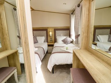 A bedroom with two single beds bedside table curtains and a dressing table with a mirror at Crosswinds 68 in Bembridge