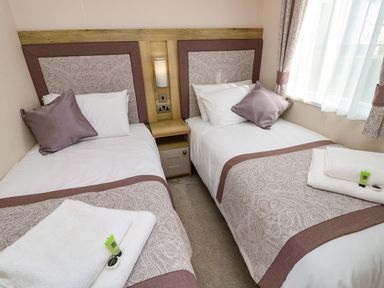 A bedroom with two single beds with cushions and towels on them at Crosswinds 68 in Bembridge