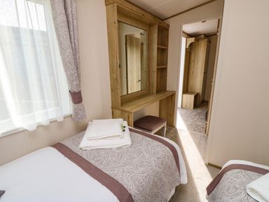 A bedroom with two single beds a wooden vanity with mirror and stool and a window with curtains at Crosswinds 68 Bembridge