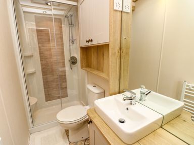 A bathroom with a shower enclosure a toilet a sink and a wooden cabinet at Crosswinds 68 in Bembridge