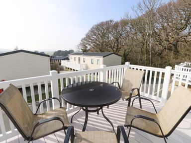 An outdoor balcony with a round black table and four beige chairs overlooking mobile homes and trees at Crosswinds 68 in Bembridge