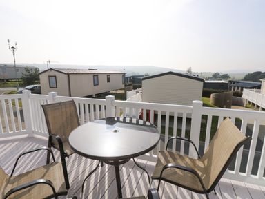 A balcony with a round table and four chairs overlooking static caravans at Crosswinds 68 in Bembridge