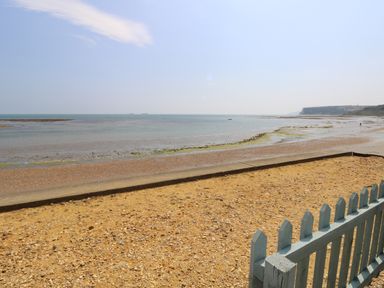 A beach with a sandy shore a blue wooden fence and a calm sea at Crosswinds 68 in Bembridge