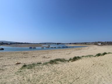 A sandy beach with grass patches and boats anchored in water with buildings in the distance at Crosswinds 68 in Bembridge