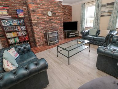 A living room with blue leather sofas a glass coffee table a brick fireplace and a bookshelf at Barnacre in Longhirst near Morpeth