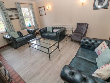 A living room with dark leather sofas a glass coffee table an accent chair and curtains at Barnacre in Longhirst near Morpeth