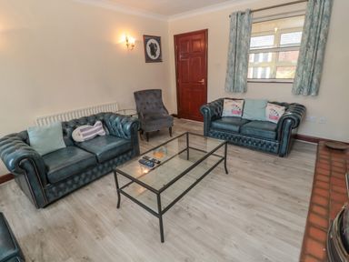 A living room with two leather sofas a glass coffee table an armchair wall sconce and a window with curtains at Barnacre Longhirst near Morpeth