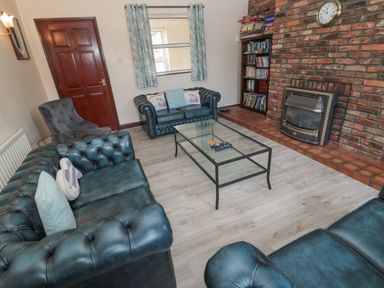 A living room with leather sofas a glass coffee table a brick fireplace and a bookshelf at Barnacre Longhirst near Morpeth