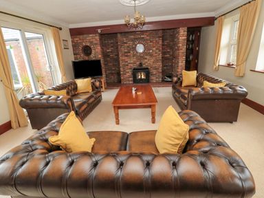 A living room with three brown leather sofas and yellow cushions around a wooden coffee table and a brick fireplace at Barnacre in Longhirst near Morpeth
