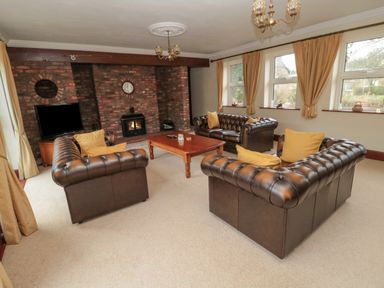 A living room with three brown leather sofas and a wooden coffee table in front of a brick fireplace with a clock above at Barnacre Longhirst near Morpeth
