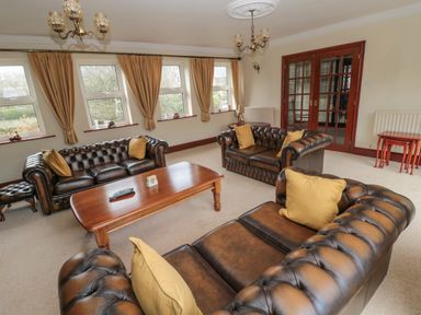 A sitting room with brown leather sofas yellow cushions wooden coffee table and windows with curtains at Barnacre Longhirst near Morpeth