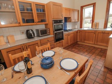 A kitchen with wooden cabinets a dining table set with plates glasses and cutlery and kitchen appliances at Barnacre in Longhirst near Morpeth