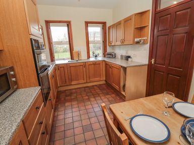 A kitchen with wooden cabinets a tiled floor a table set with two plates and glasses at Barnacre in Longhirst near Morpeth