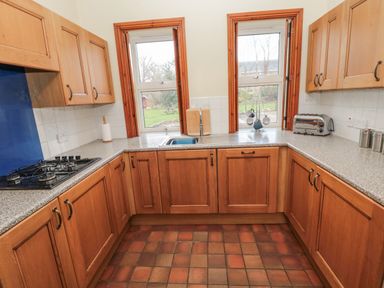 A kitchen with wooden cabinets granite countertops a gas stove a sink and two windows at Barnacre in Longhirst near Morpeth