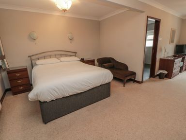 A bedroom with a double bed armchair wooden nightstands and a dresser with a television at Barnacre in Longhirst near Morpeth