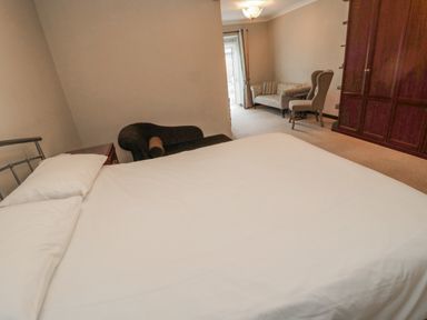 A bedroom with a bed white bedding a sofa armchair a wardrobe and a window at Barnacre in Longhirst near Morpeth