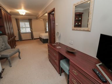 A bedroom with a wardrobe and chair a dressing table with a mirror and television at Barnacre in Longhirst near Morpeth