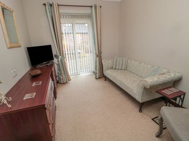 A sitting room with a patterned sofa cushions a wooden dresser with a television and striped curtains at Barnacre in Longhirst near Morpeth